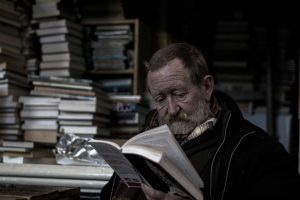 Man reading a book, surrounded by stacks of books,